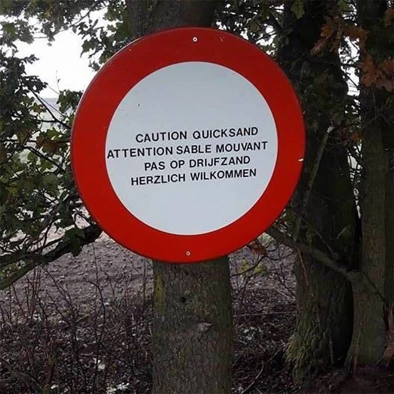 Ein Schild, das in drei Sprachen vor Treibsand warnz und als deutschen Text "herzlich wilkommen" stehen hat. 