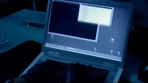 A pair of gloved hands typing on a silver mid-2000s laptop, running KDE 2 with a grey theme. Two windows are open: KFM and an unidentified video player.